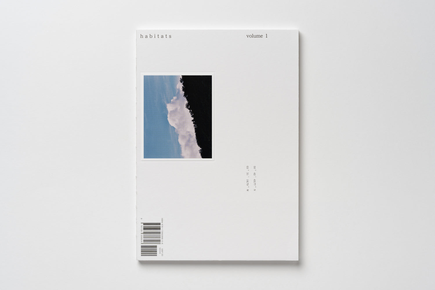 A photo of Habitats Volume 1's front cover, with an inset photo of puffy white clouds and dark trees against a blue sky. Small typographic details surround the inset photo on the cover.